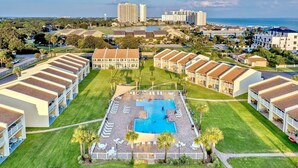 A resort with multiple-story buildings, a central swimming pool, and a view of the ocean.