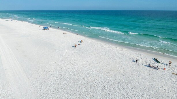 A wide sandy beach with clear turquoise water, a few umbrellas, and people enjoying the beach.