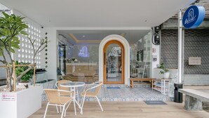Un espacio al aire libre con sillas de mimbre, una mesa pequeña, un banco de madera y una planta en maceta.