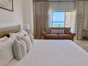 A hotel room with a large bed, a sofa, and a view of the sea.