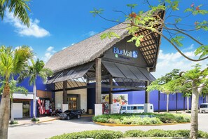 A BlueMall building with a thatched roof, palm trees, and a parking area. - Beautiful beachfront penthouse at Cap Cana (Punta Cana)