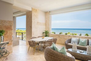 A balcony with a view of the sea, wicker furniture, and a table with a bowl of fruit.