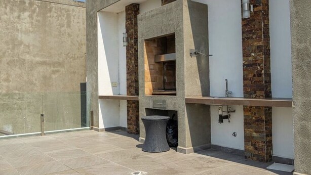 A modern outdoor kitchen area with a built-in grill, a small round table, and a glass enclosure. - Luxurious stay at modern apartment Equipetrol (Santa Cruz de la Sierra)