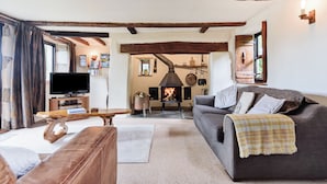 Ein gemütliches Wohnzimmer mit Kamin, einer Couch, einem Fernseher und Holzbalken an der Decke.