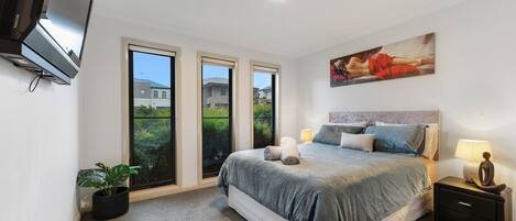 A bedroom with a bed, a nightstand, a TV, and a window with a view of greenery.