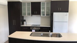 Une cuisine moderne avec des meubles de couleur sombre, un réfrigérateur blanc et un évier en acier inoxydable.