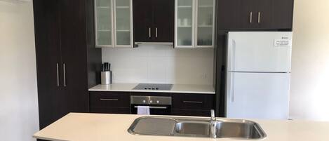 A modern kitchen with dark cabinets, a white refrigerator, and a stainless steel sink.