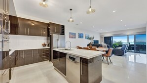 Een moderne keuken met een centraal eiland, roestvrijstalen apparatuur en hangende lampen.