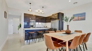 Een moderne keuken met donkere kastjes, een centraal kookeiland met barkrukken, en een eethoek met een houten tafel en leren stoelen.
