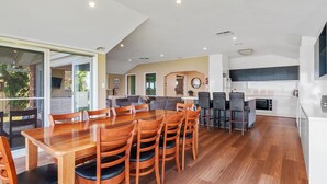 Un vaste espace de vie comprenant un coin repas avec table et chaises, une cuisine et une grande porte-fenêtre coulissante donnant sur un espace extérieur.