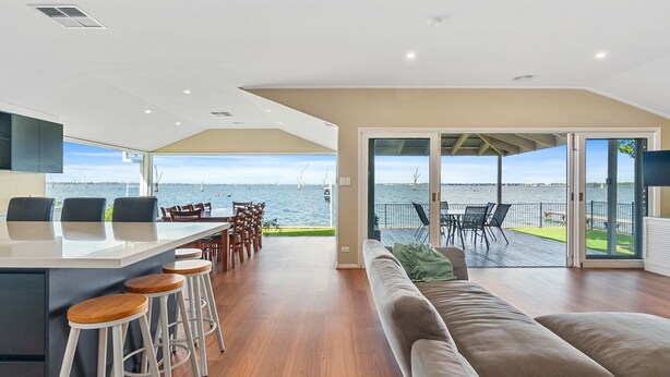 Un intérieur moderne comprenant une cuisine, un coin repas et un balcon avec vue sur l’eau.