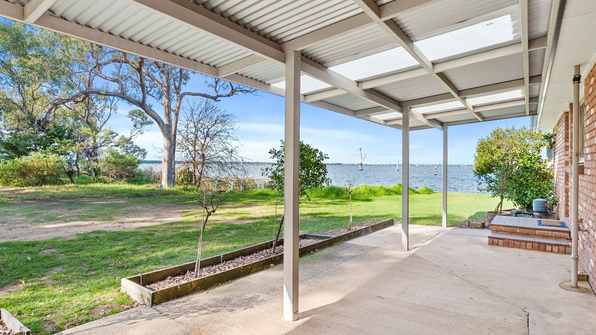 A covered outdoor area with a view of the water, concrete flooring, and a brick wall.