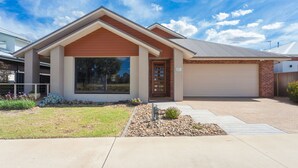 Une maison moderne de plain-pied, dotée d’un garage, d’une grande fenêtre à l’avant et d’un jardin bien entretenu, agrémenté d’un petit parterre de fleurs et d’un chemin menant à la porte d’entrée.