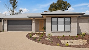 Een modern huis met twee verdiepingen, een garage, een groot raam en een verzorgde tuin.