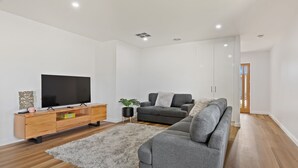 Een moderne woonkamer met een flatscreen televisie, een houten tv-meubel, een grijze bank en een zacht tapijt.