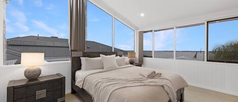 A bedroom with a large bed, a nightstand, a lamp, and a view of the beach.