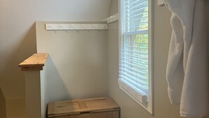 Un baño con un banco de madera, un perchero, un reloj y una ventana con persianas.