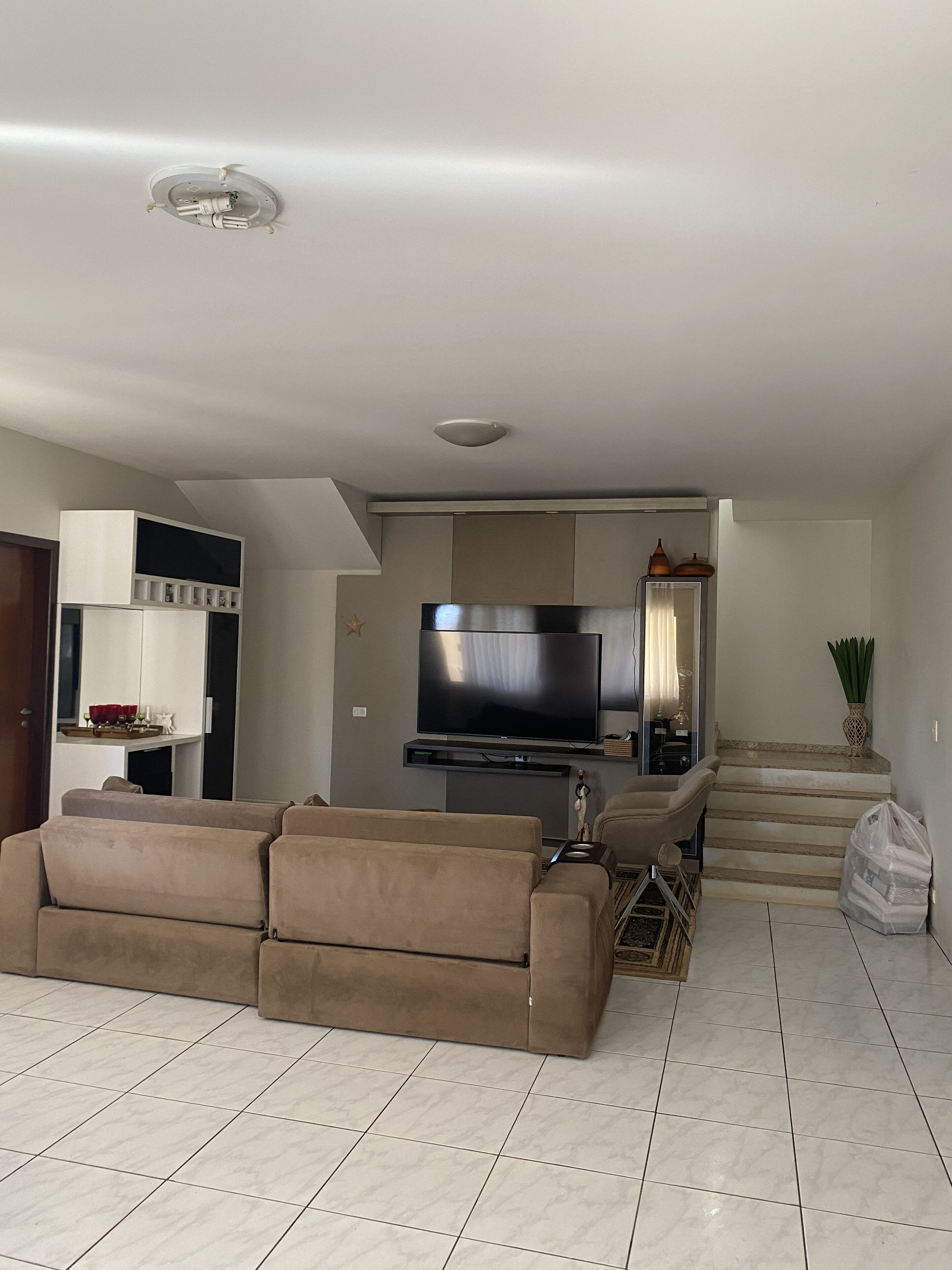 A modern living room with a beige sofa, a flat-screen TV, and a staircase leading to an upper level.