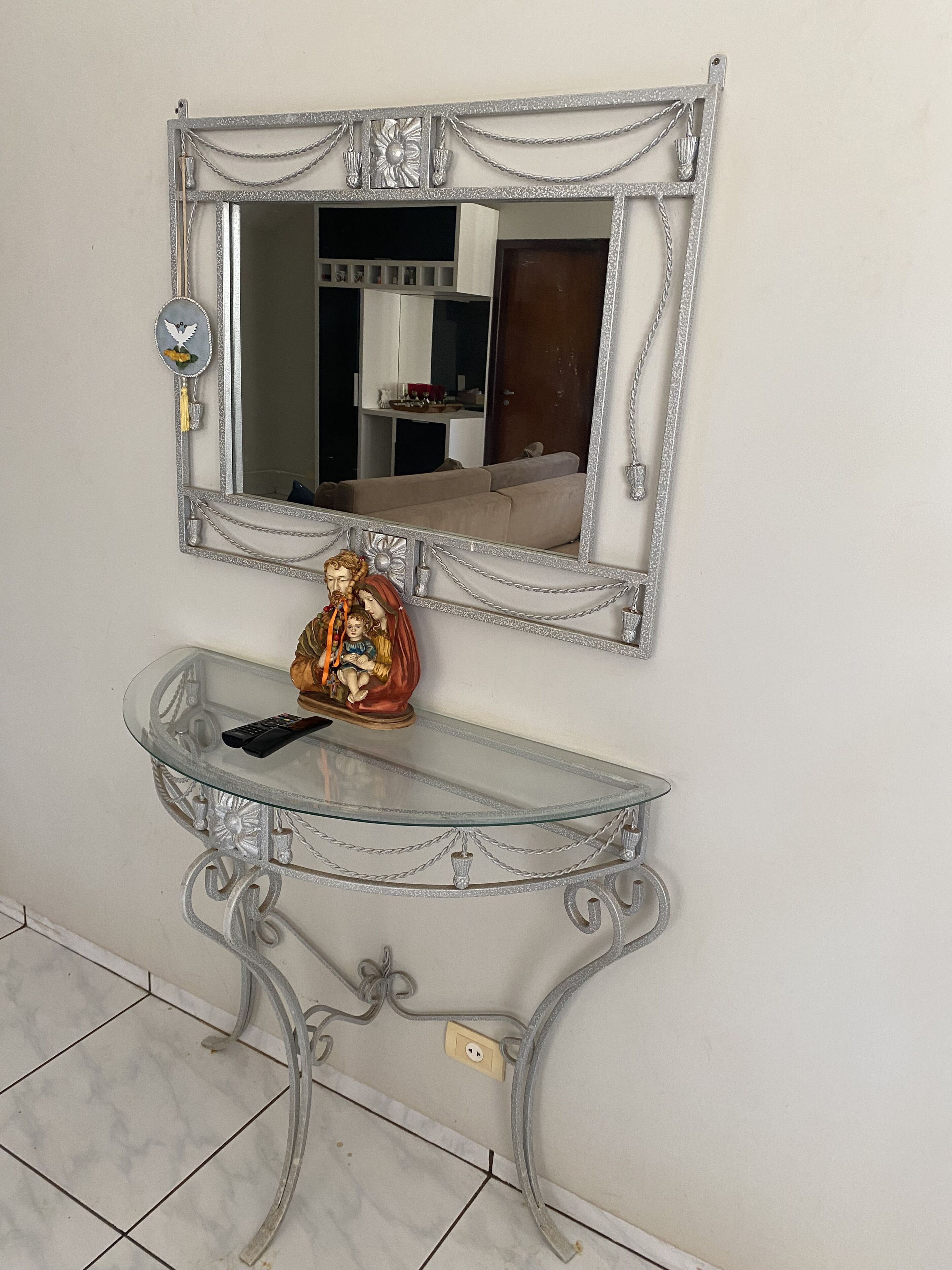 A mirror with a decorative frame, a glass console table, and a small statue.