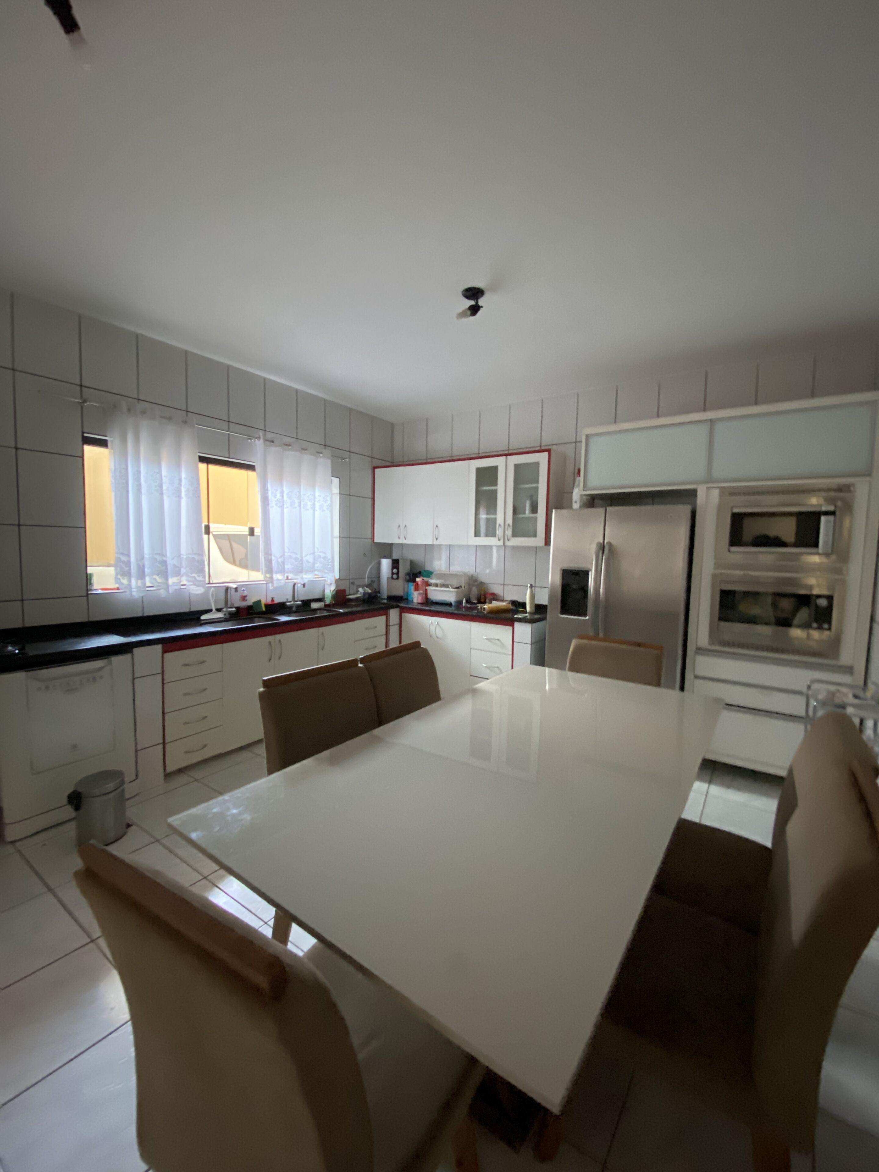 Une cuisine moderne avec des meubles blancs, une table à manger et un réfrigérateur.