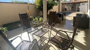 Un patio al aire libre con sillas y mesas de metal, techo cubierto y vistas de los edificios circundantes.