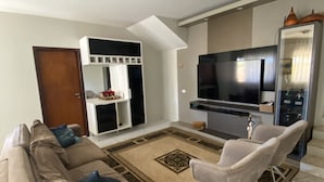Una sala de estar con sofá, televisor y un comedor con sillas.