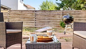 Een terras buiten met rieten meubels, een barbecue en een tafel gedekt voor een maaltijd.