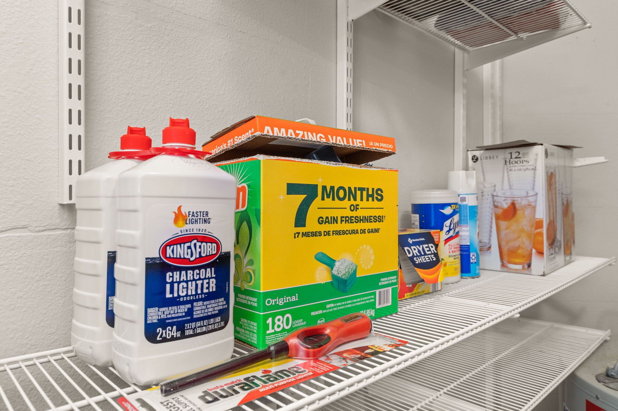 En hyld med diverse rengøringsprodukter, herunder en stor beholder med Kingsford Charcoal Lighter, en kasse med 7 måneders friskhed og en kasse med Libby 12 timer.