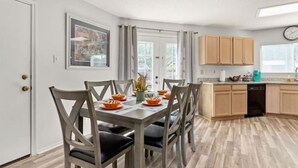 Een moderne keuken met houten kastjes, een eettafel met stoelen en een klok aan de muur.
