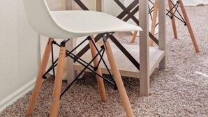 Een kamer met een kleine tafel en twee witte stoelen met houten poten. Op de tafel staat een plant in een pot.