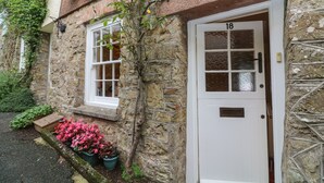 Ein Steinhaus mit einer weißen Tür, auf der „18“ steht, und einem Fenster mit weißen Rahmen.
