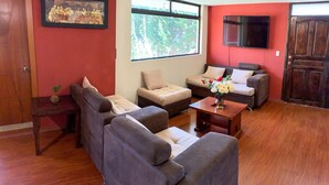 Un salon avec un mur rouge, une grande fenêtre, un téléviseur à écran plat et un plancher en bois.