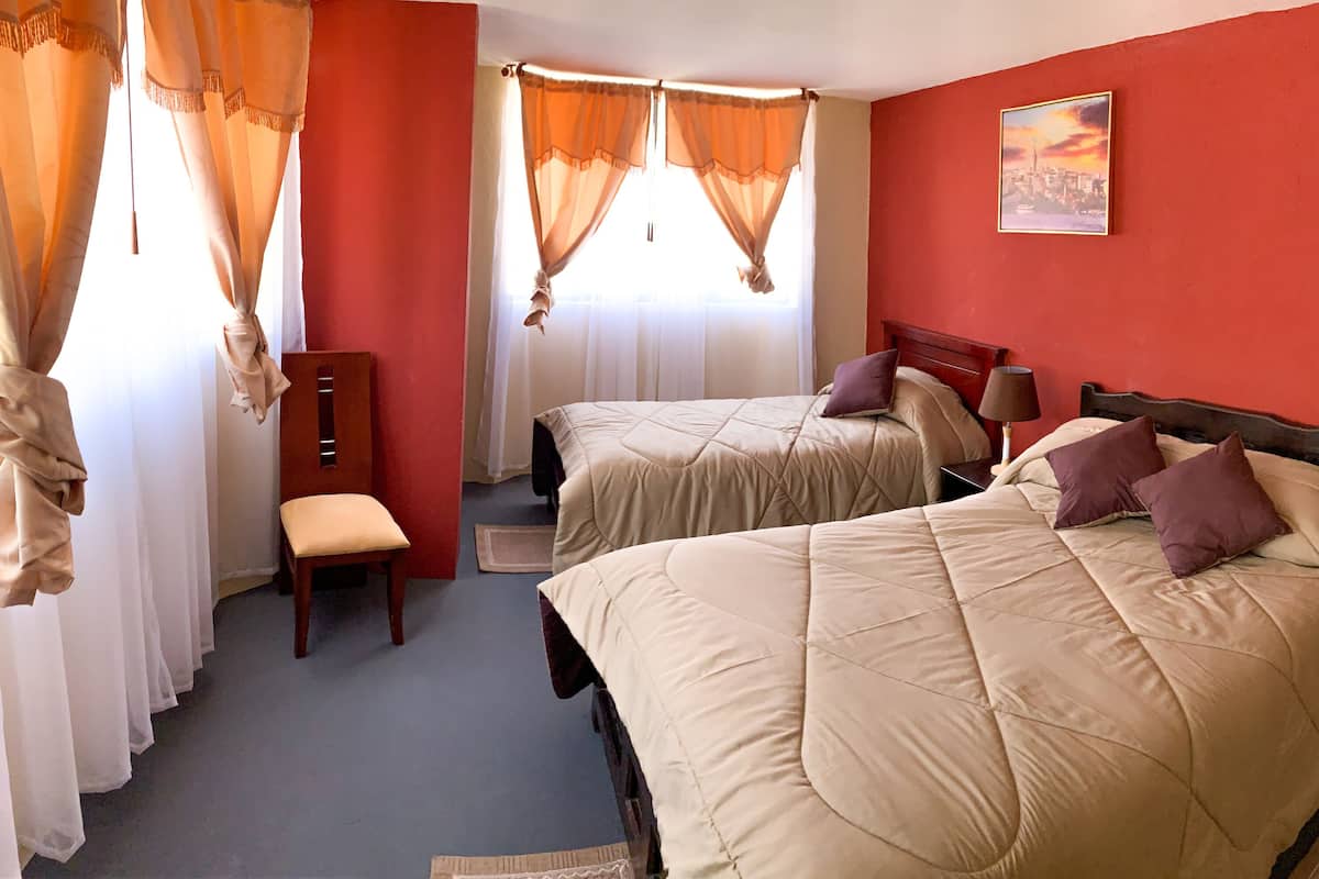 Habitación de hotel con dos camas, una silla, un escritorio y una ventana con cortinas.