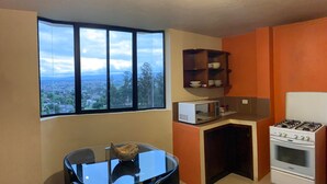 Une cuisine compacte comprenant une table à manger, un four à micro-ondes, une cuisinière et offrant une vue sur le paysage urbain grâce à de grandes fenêtres.