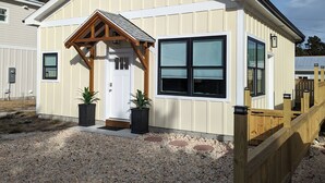 A single-story building with a gabled roof, a front door, and a small porch with wooden beams. - Coastal Cottage, walk to downtown Beaufort, close to beaches, pet friendly. (Beaufort)