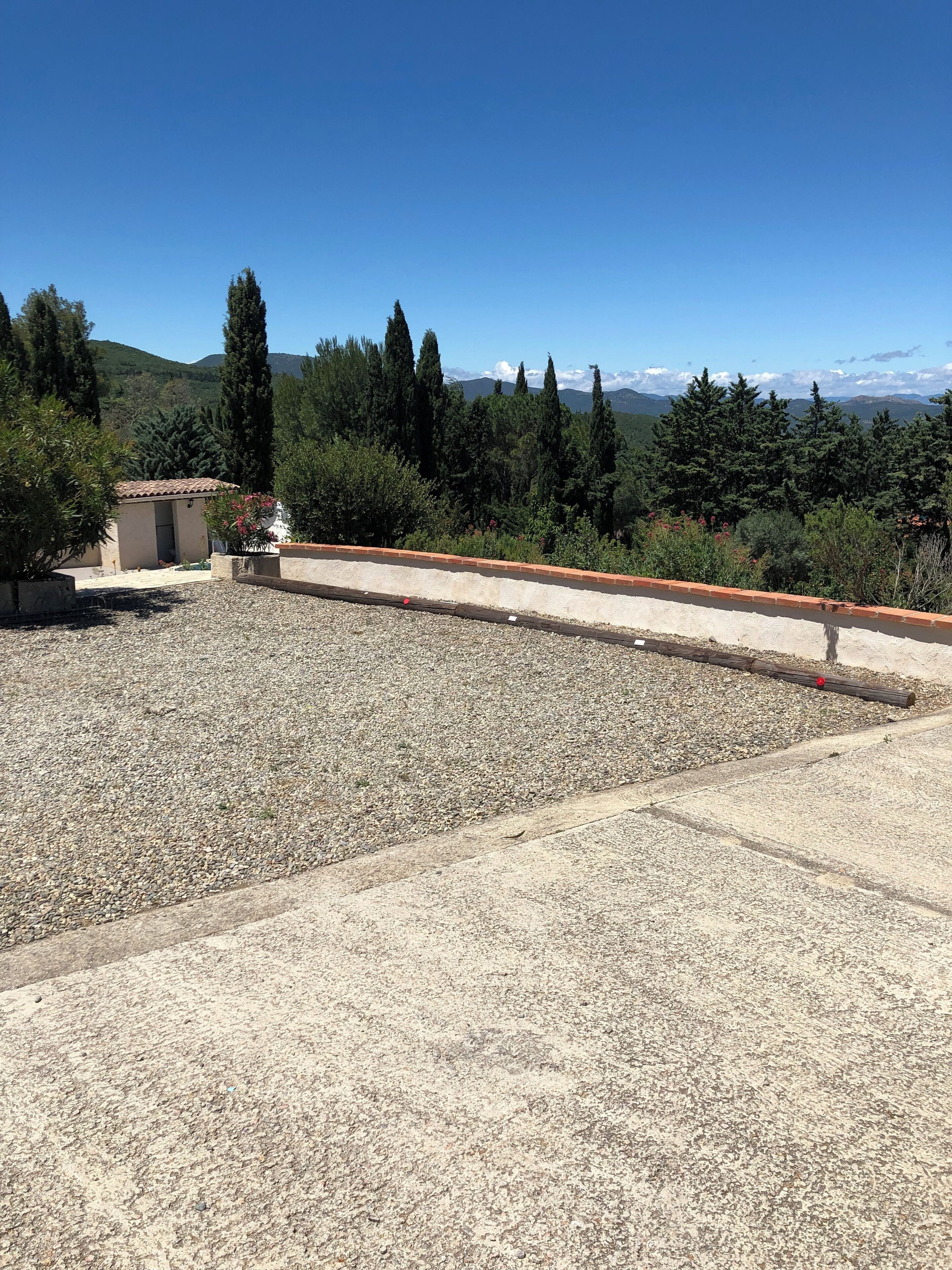 Eine Dachterrasse mit Kiesboden, einem kleinen Gebäude und Blick auf Bäume und Berge.