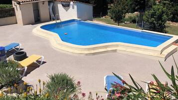 Una piscina con solárium de baldosas, rodeada de sillas de descanso y un pequeño edificio con tejado de cerámica.