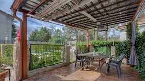 Un patio couvert avec une table et des chaises, une vue sur un espace vert et un pilier en pierre.