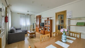 Un salon comprenant un canapé, une table à manger, des chaises, un téléviseur et une bibliothèque.