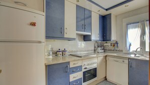 Une cuisine avec des meubles blancs et bleus, un réfrigérateur, un four, un lave-vaisselle et un évier.
