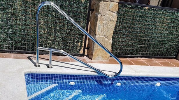 Une piscine avec une eau d’un bleu limpide, une échelle en métal et un mur de pierre en arrière-plan.