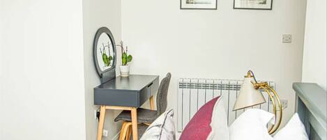 A bedroom with a bed, a desk, a chair, a radiator, and two framed pictures on the wall.