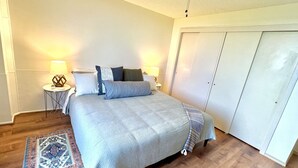 A bedroom with a bed, two bedside tables, a ceiling fan, a nightstand, a rug, and a wardrobe. - Incredible View in Hilo - Pool, A/C, #708 (Hilo)
