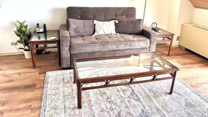 A living room with a grey sofa, a glass coffee table, a wooden side table, a floor lamp, and a radiator. - Incredible View in Hilo - Pool, A/C, #708 (Hilo)