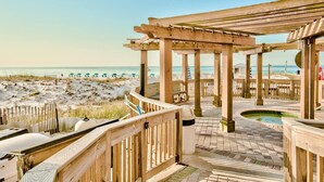 A wooden deck with a pool, beach views, and a covered area with columns. - Renovated Beachfront Condo with Sensational Views! (Destin)