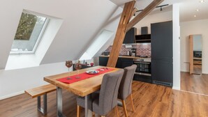 A modern loft apartment with a dining area featuring a wooden table and bench, a kitchen with a brick backsplash, and a large skylight.