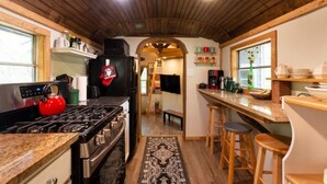 A kitchen with a stove, oven, and red kettle. There are wooden stools and a bar counter. - Bluebird Nest (San Marcos)