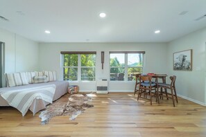 A room with a bed, a dining table with chairs, a large window, and a ceiling light.