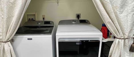 Un área de lavandería con dos lavadoras Maytag, un estante con toallas dobladas y una botella roja de detergente.