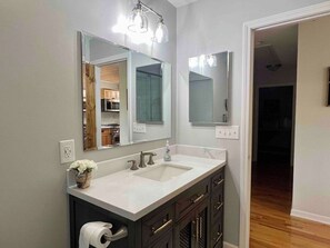 A bathroom with a double sink, dark cabinetry, a mirror, and a light fixture above the mirror. - Mtn View, Fire Pit+Grill, WiFi! Nearby Town & AVL! (Burnsville)